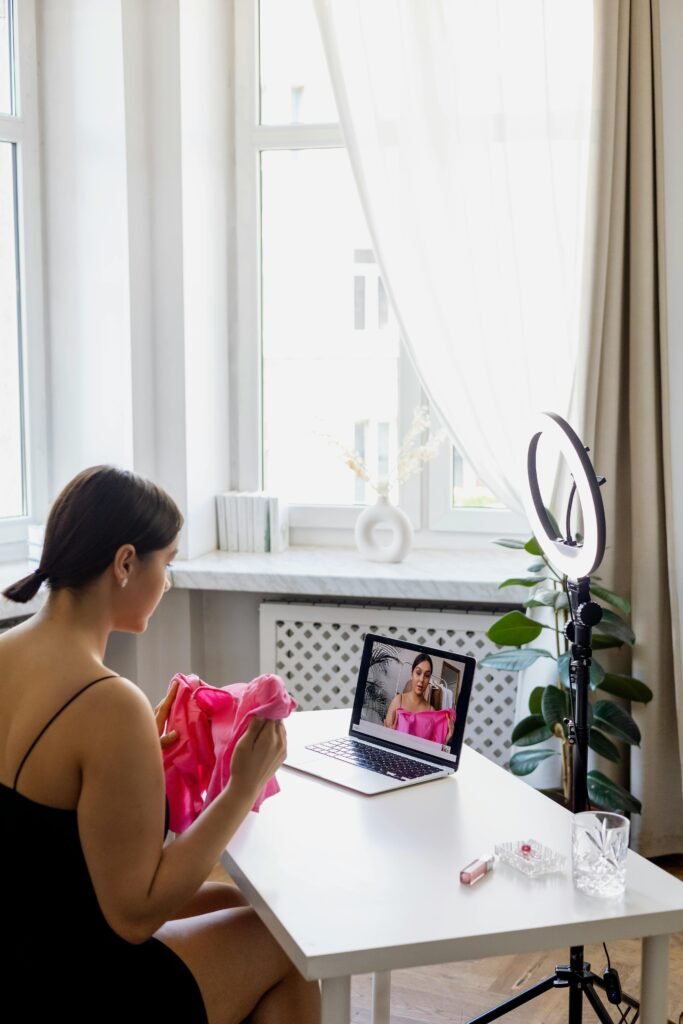 A young woman creates fashion vlog content at home with a laptop and ring light.